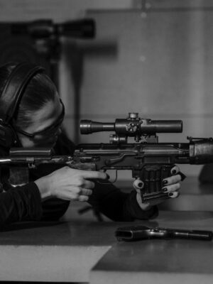 Woman aiming rifle in shooting range. Black and white focus on precision and skill.